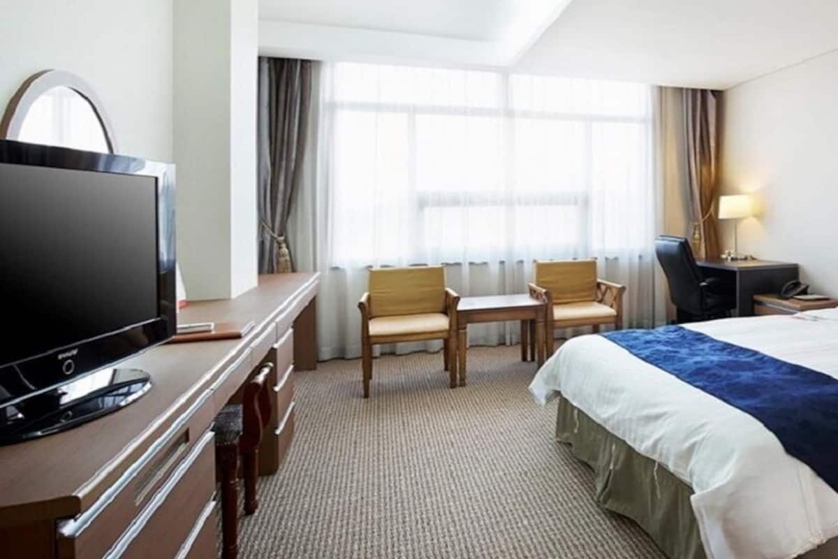 Une chambre d’hôtel avec un grand lit, un bureau avec une télévision, une chaise et une lampe de bureau.