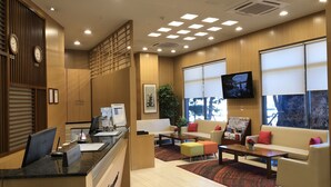 Een hotel lobby met een receptiebalie, een zithoek en grote ramen.