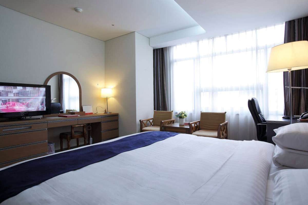 Une chambre d’hôtel équipée d’un lit, d’un bureau, d’une chaise, d’une télévision, d’une lampe et de grandes fenêtres.