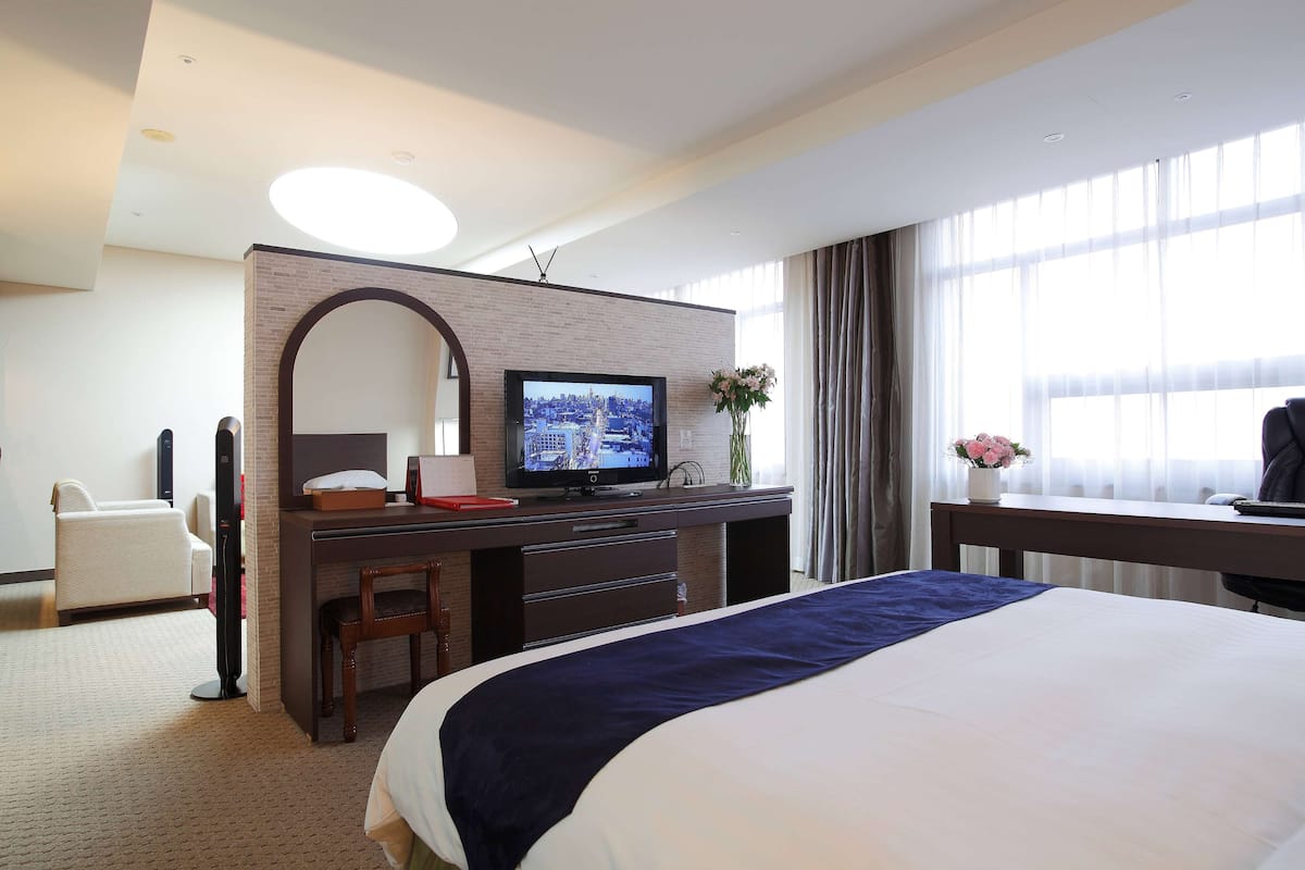 Une chambre d’hôtel avec un grand lit, un bureau doté d’un téléviseur à écran plat, une chaise, une petite table et un vase avec des fleurs.