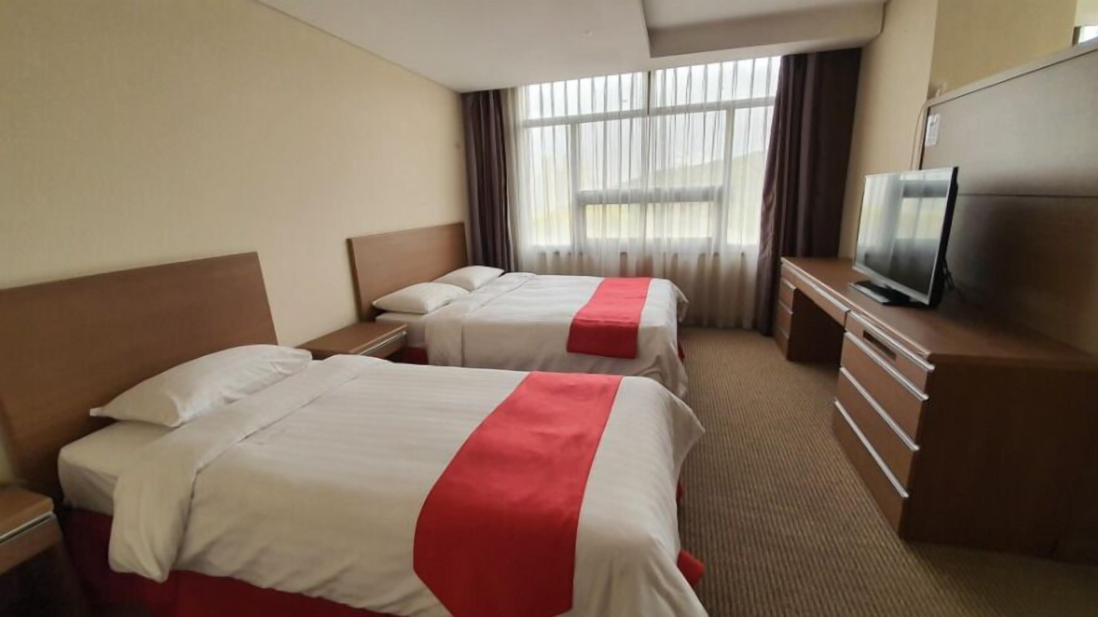 Een hotelkamer met twee bedden, een televisie, een kaptafel en een raam met gordijnen.