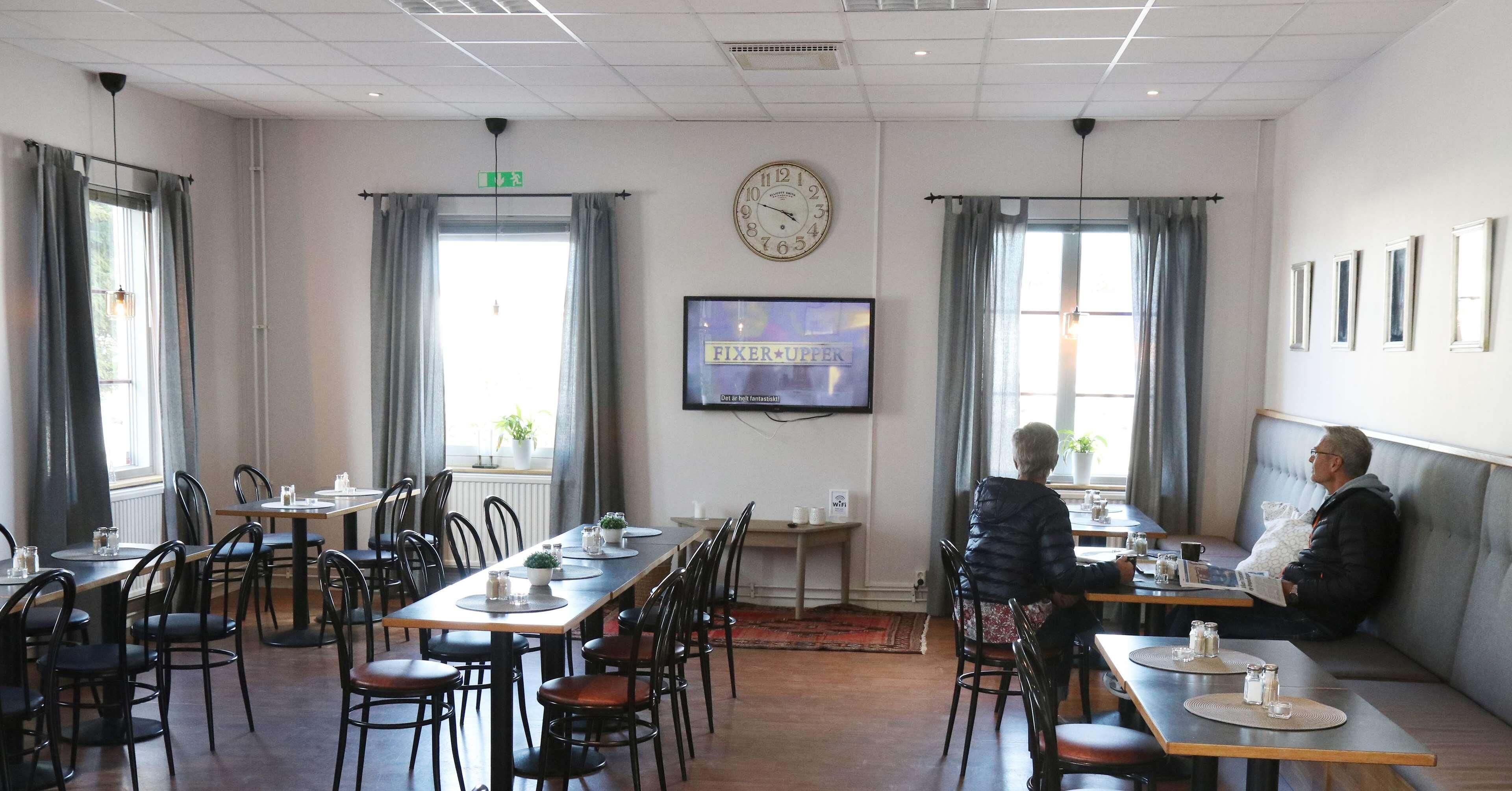 Un comedor con mesas, sillas, un reloj y una pantalla de televisión mostrando 