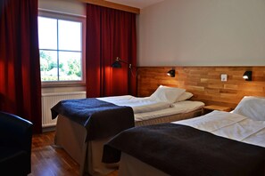 A hotel room with two beds, a window with curtains, a wooden headboard, and a bedside table with a lamp.
