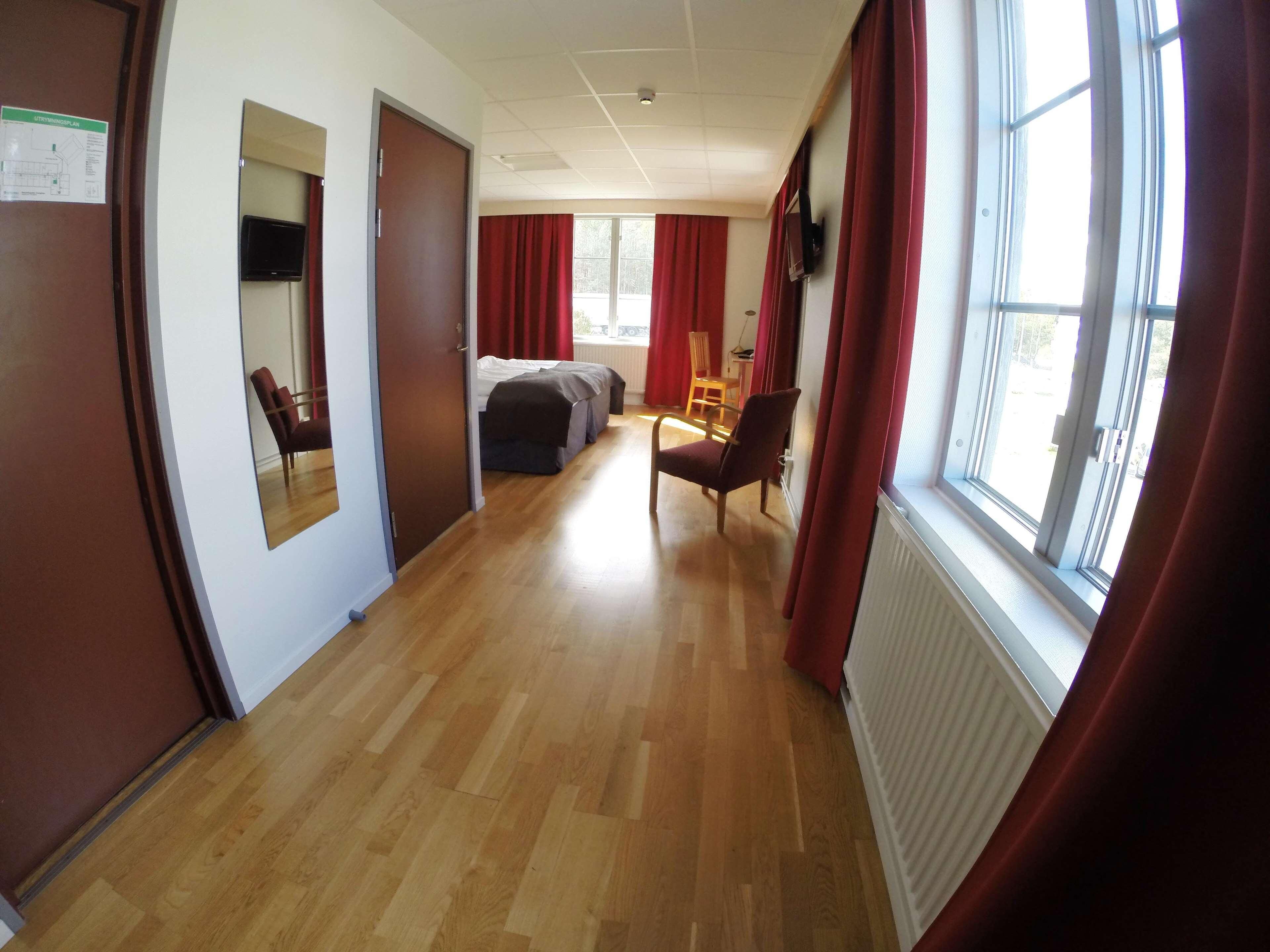 A hallway with wooden flooring, red curtains, a bed, a chair, and a radiator.