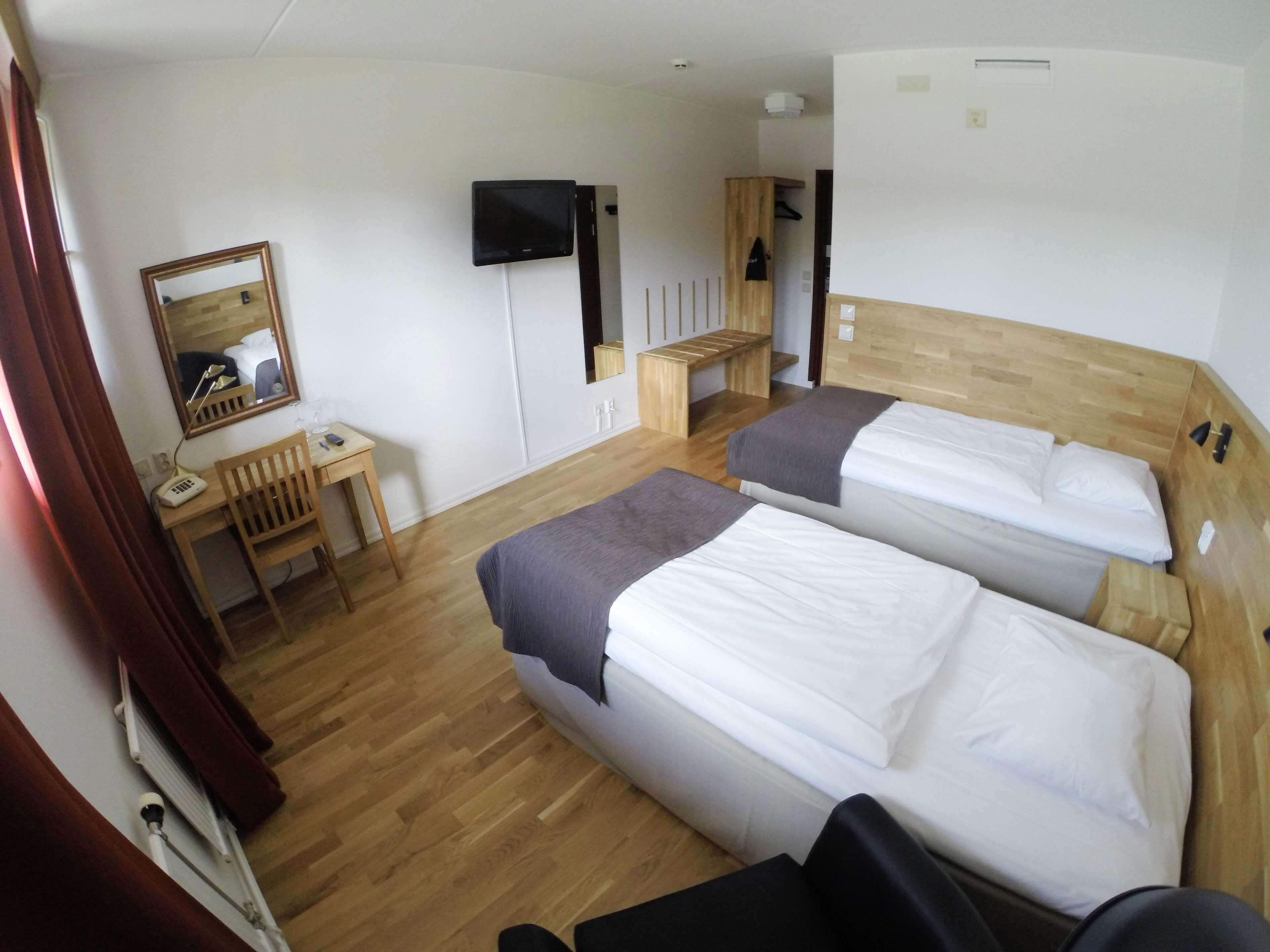 Habitación de hotel con dos camas, un escritorio, una silla, un televisor y un espejo.