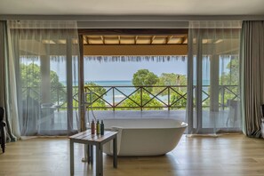 Una habitación con una bañera grande, una mesa con artículos de aseo y vistas al mar y al follaje.