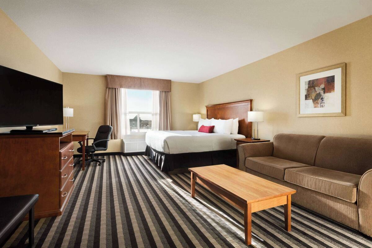 Una habitación de hotel con una cama, un sofá, un escritorio con televisor, una silla y una mesita de centro.
