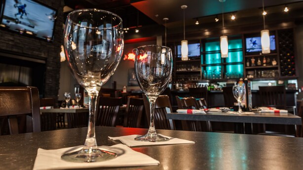 Un coin bar avec deux verres à vin vides posés sur une table, un écran de télévision en arrière-plan et un meuble à bouteilles.
