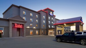 Un hôtel avec un toit plat, un parking et un panneau lumineux au néon indiquant « Ricky's All Day Grill ».