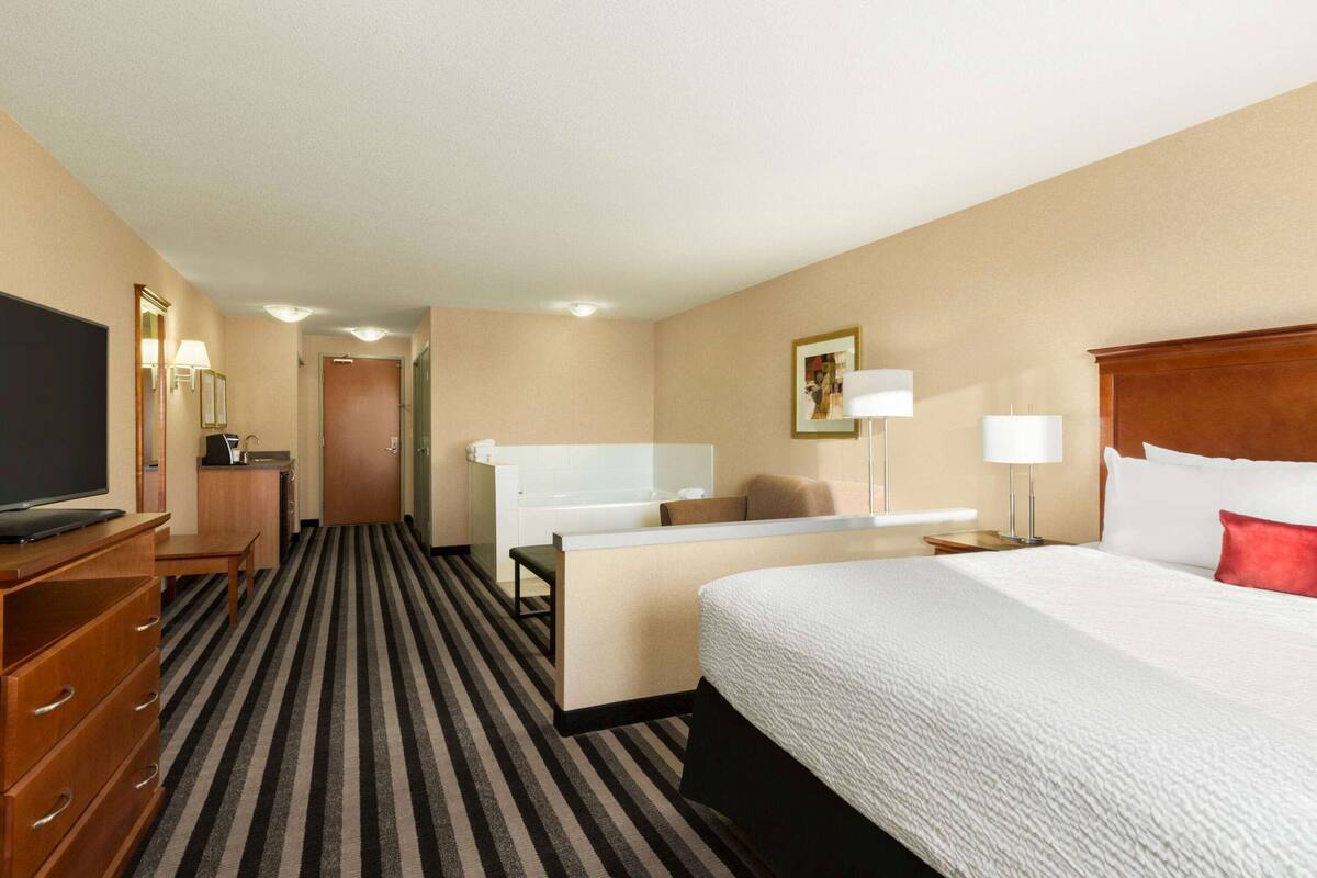 Una habitación de hotel con cama, escritorio, televisor, cómoda y baño.