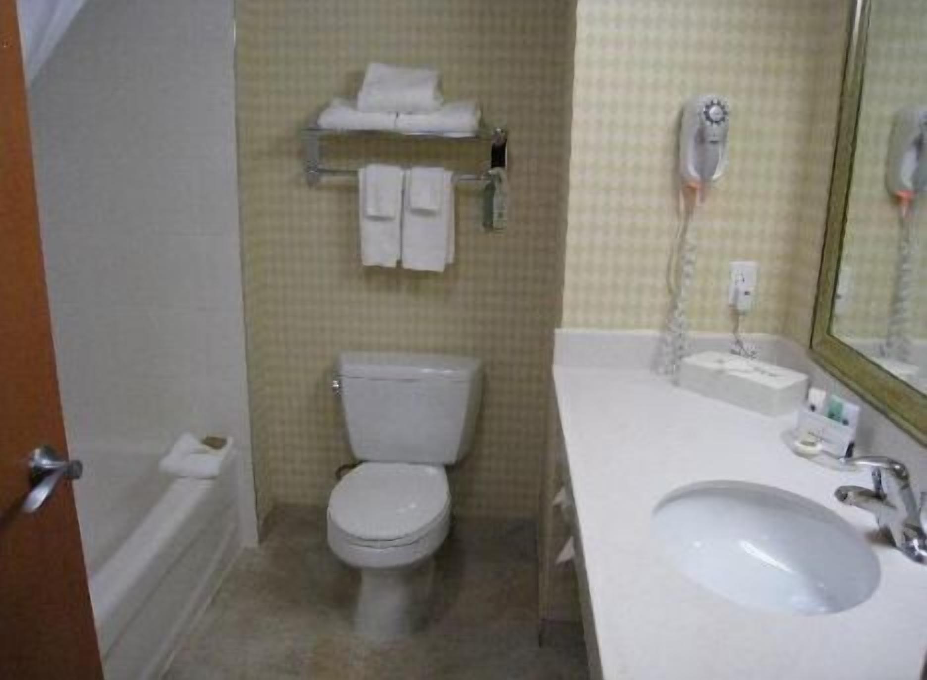 Un baño con inodoro, lavamanos y toallero con toallas.