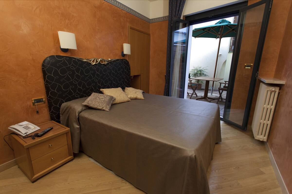 A bedroom with a bed, a nightstand, a telephone, and a sliding glass door leading to an outdoor patio.