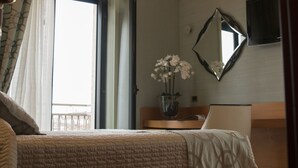 Habitación de hotel con una cama, una mesita de noche con un florero y un espejo, además de un televisor en la pared.