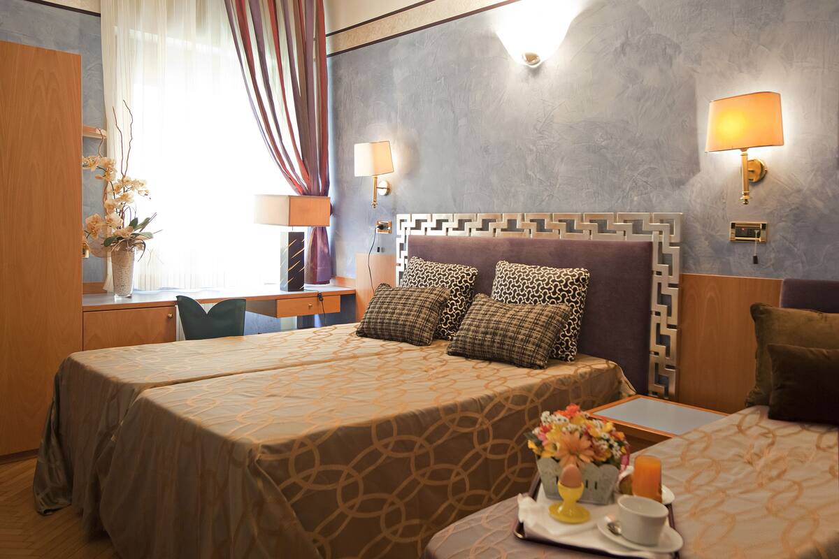A hotel room with two beds, a desk, a chair, and a window with curtains.