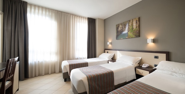 Habitación de hotel con dos camas, un escritorio y una silla. Hay un cuadro en la pared y una ventana con cortinas.
