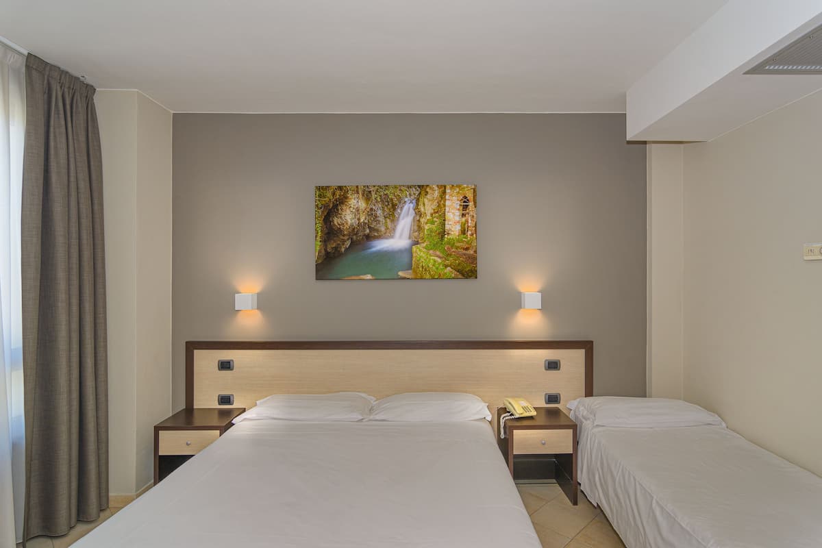 Habitación de hotel con una cama grande, otra más pequeña, dos mesitas de noche, un teléfono y un cuadro de una cascada en la pared.