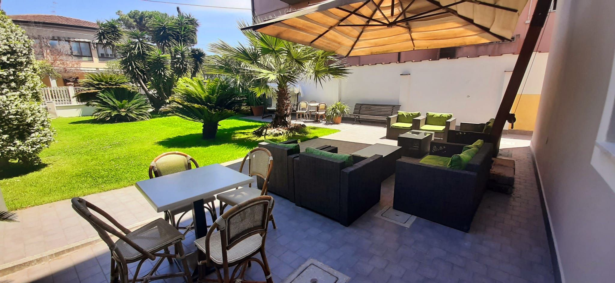 Eine Terrasse im Freien mit Tisch und Stühlen, einer Sitzecke und einem großen Sonnenschirm.