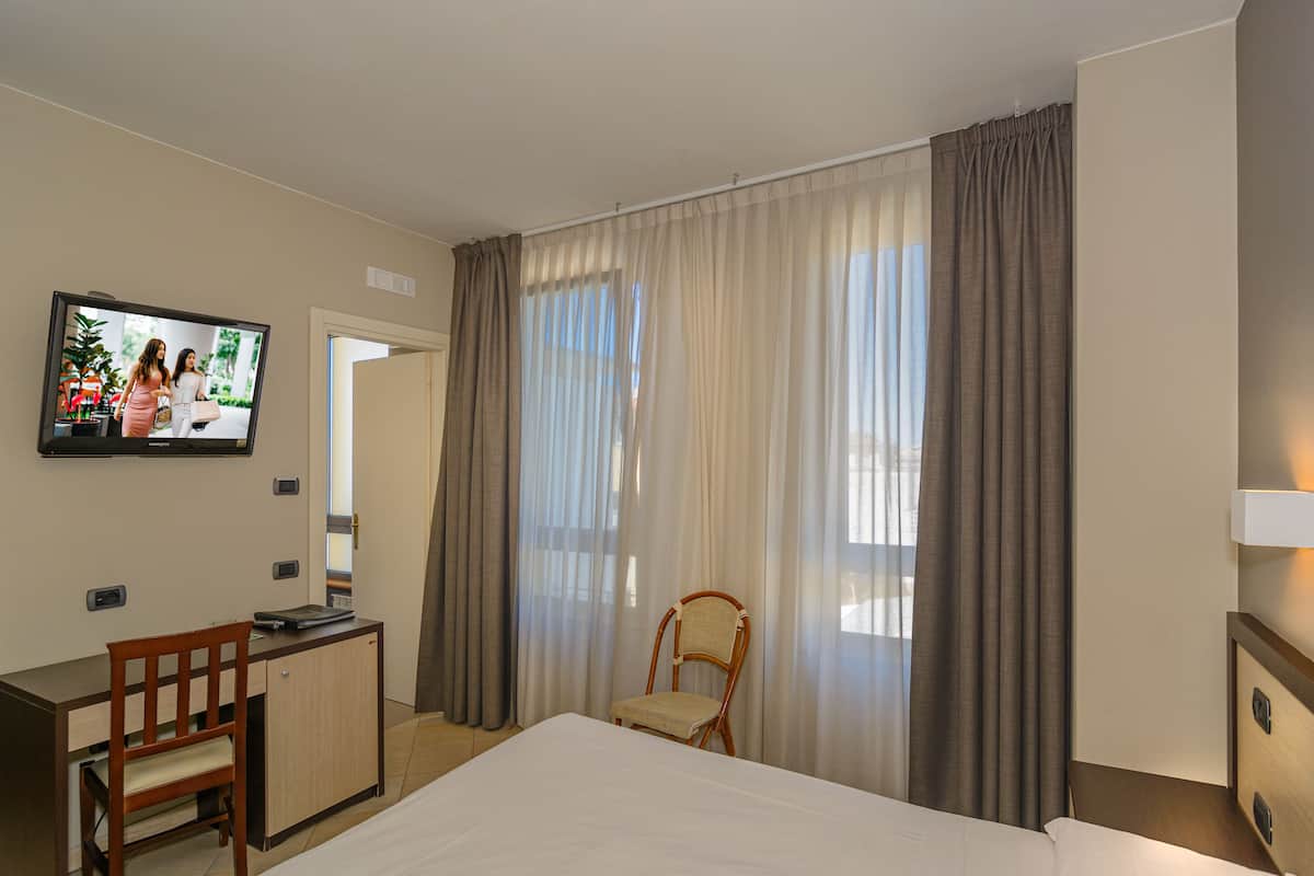 Una habitación de hotel con cama, escritorio, silla, televisor y cortinas.