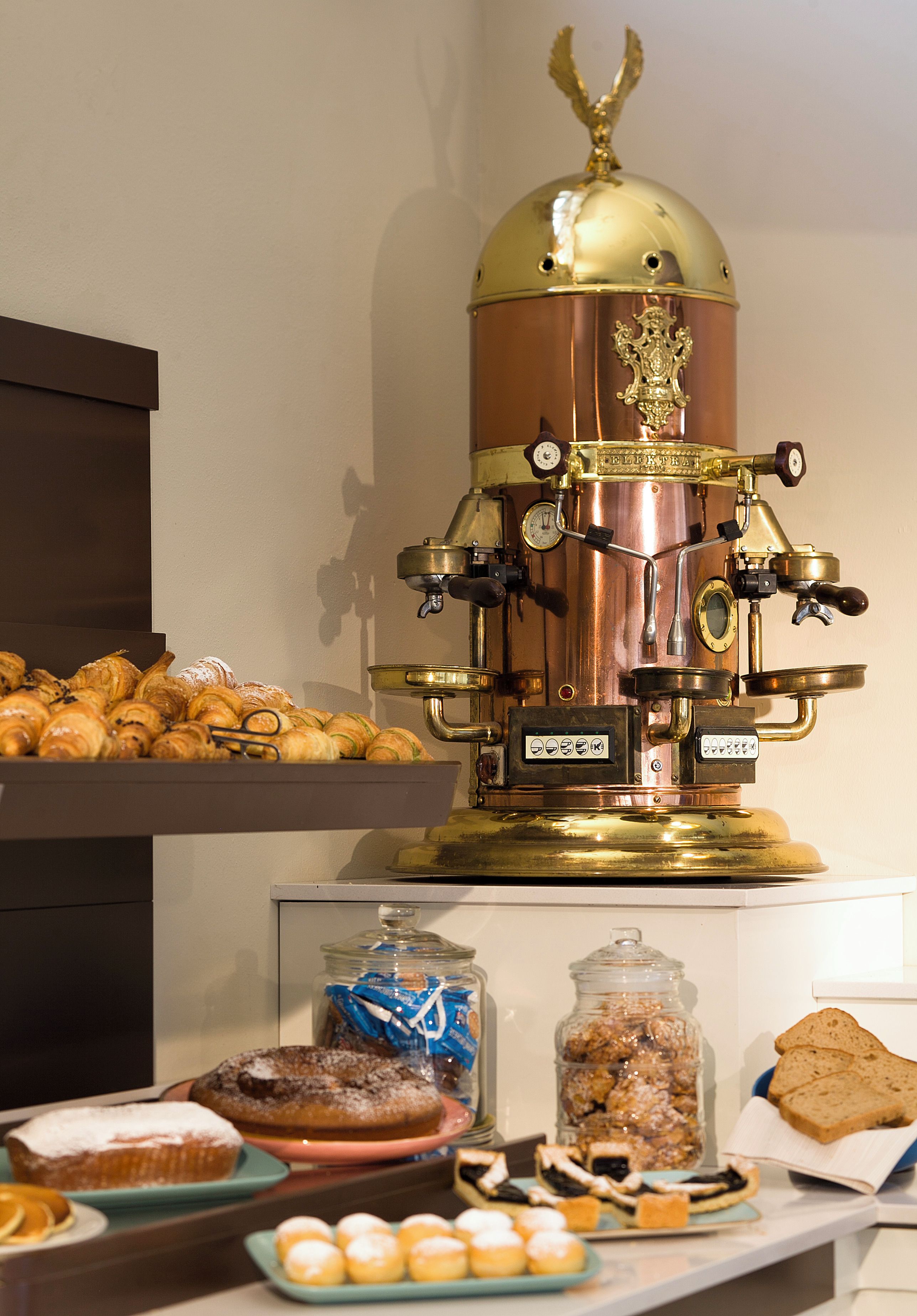 A buffet setup with a coffee machine, pastries, and various food items.