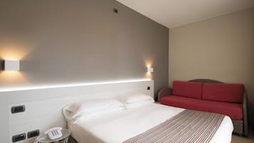 Ein Hotelzimmer mit einem Bett, einem Nachttischtelefon, einer Wandleuchte und einem roten Sofa.