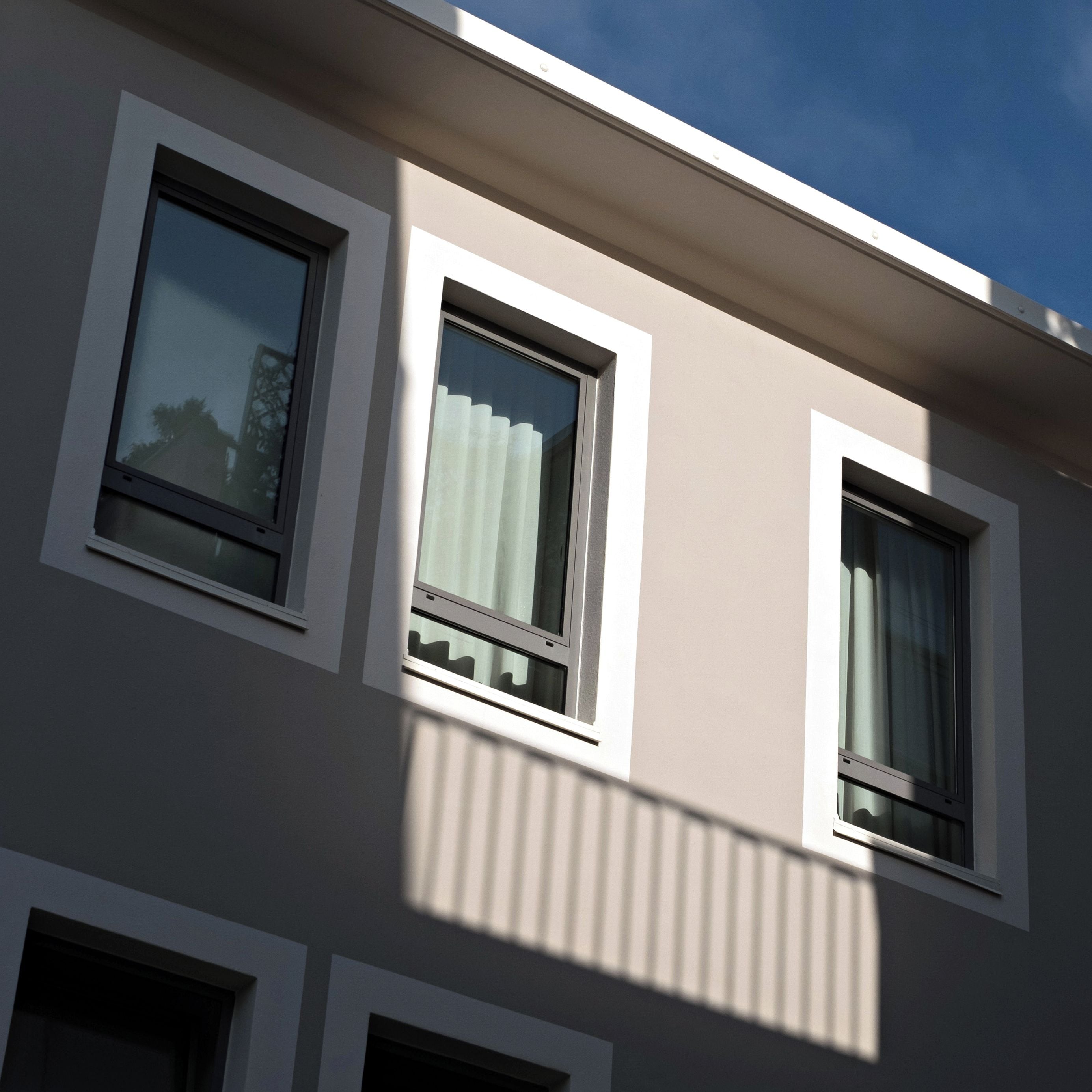 A building with three windows, each with a white frame and a curtain.