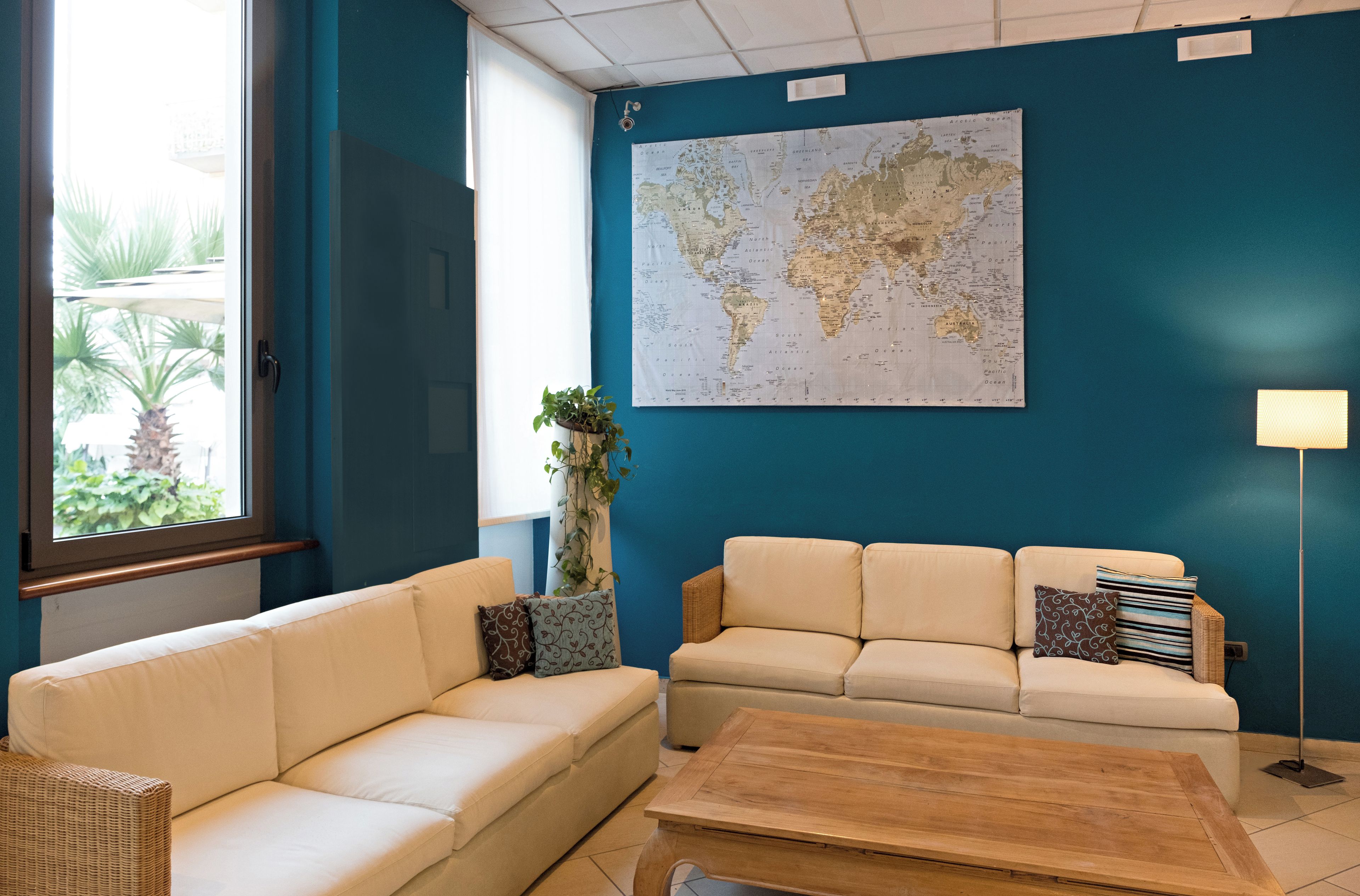A room with two beige sofas, a wooden coffee table, a world map on the wall, and a potted plant.