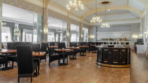 A spacious dining area with multiple tables and chairs, a central bar area, and large windows allowing natural light. - The Clifton Hotel (Scarborough)