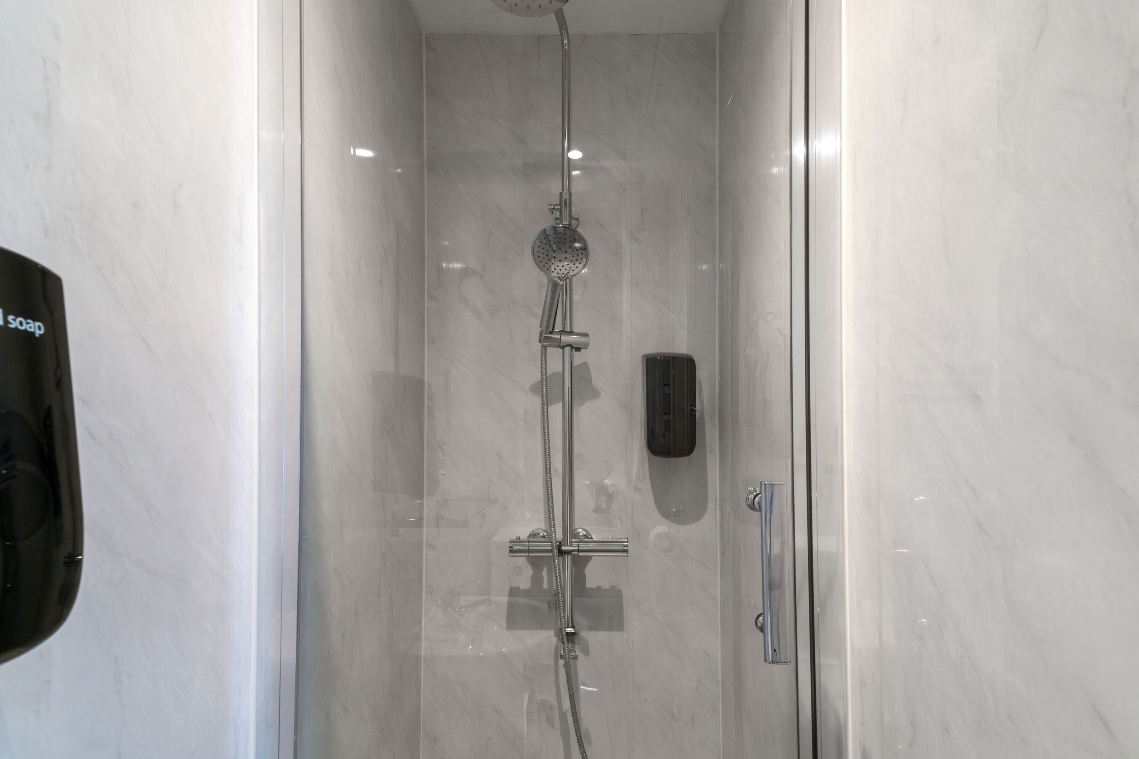 Une salle de bain moderne dotée d’une douche à parois de verre, d’un pommeau de douche à main et d’un distributeur de savon.