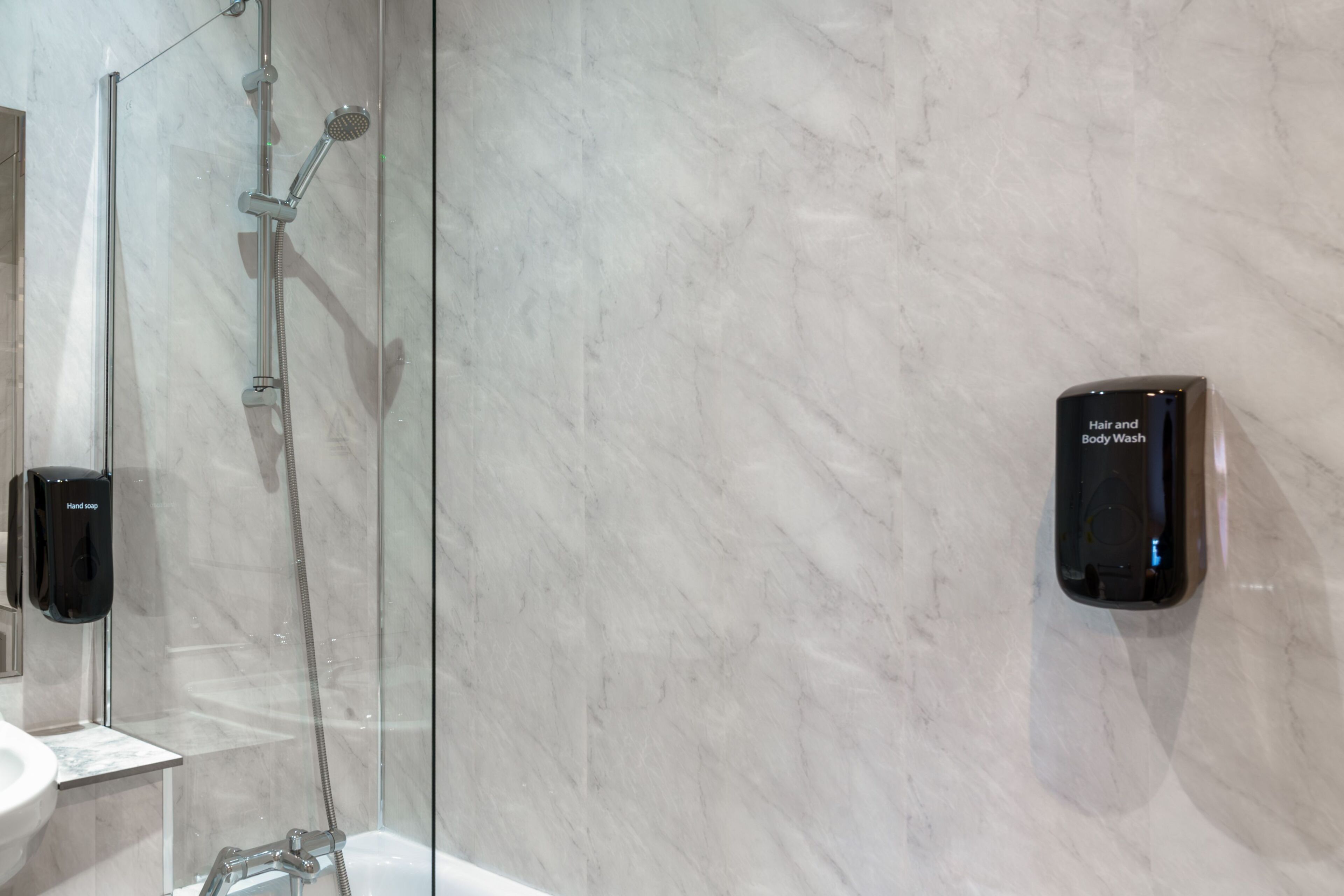 A modern bathroom with a glass-enclosed shower, a hand soap dispenser, and a wall-mounted hair and body wash station.