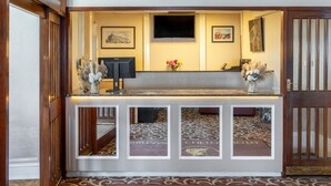 A reception desk with a flat-screen TV, framed artwork, and a welcome mat. - The Clifton Hotel (Scarborough)