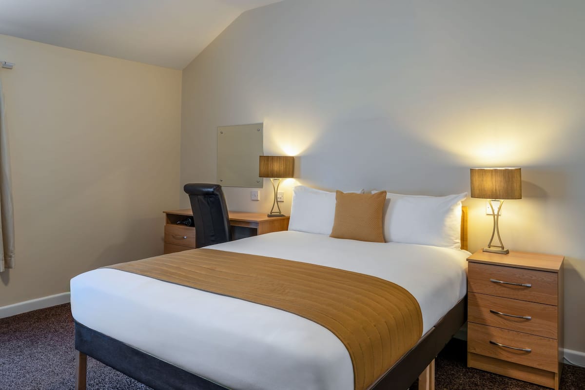 A hotel room with a bed, bedside tables, a desk, a chair, and a mirror.