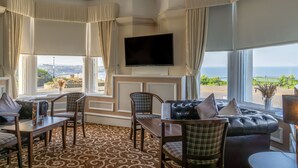 A room with a large TV, a sofa, chairs, a dining table, and a view of the ocean. - The Clifton Hotel (Scarborough)