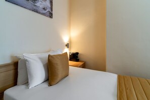 Een hotelkamer met een bed, kussens, een nachtkastje met een lamp en een wanddecoratie.