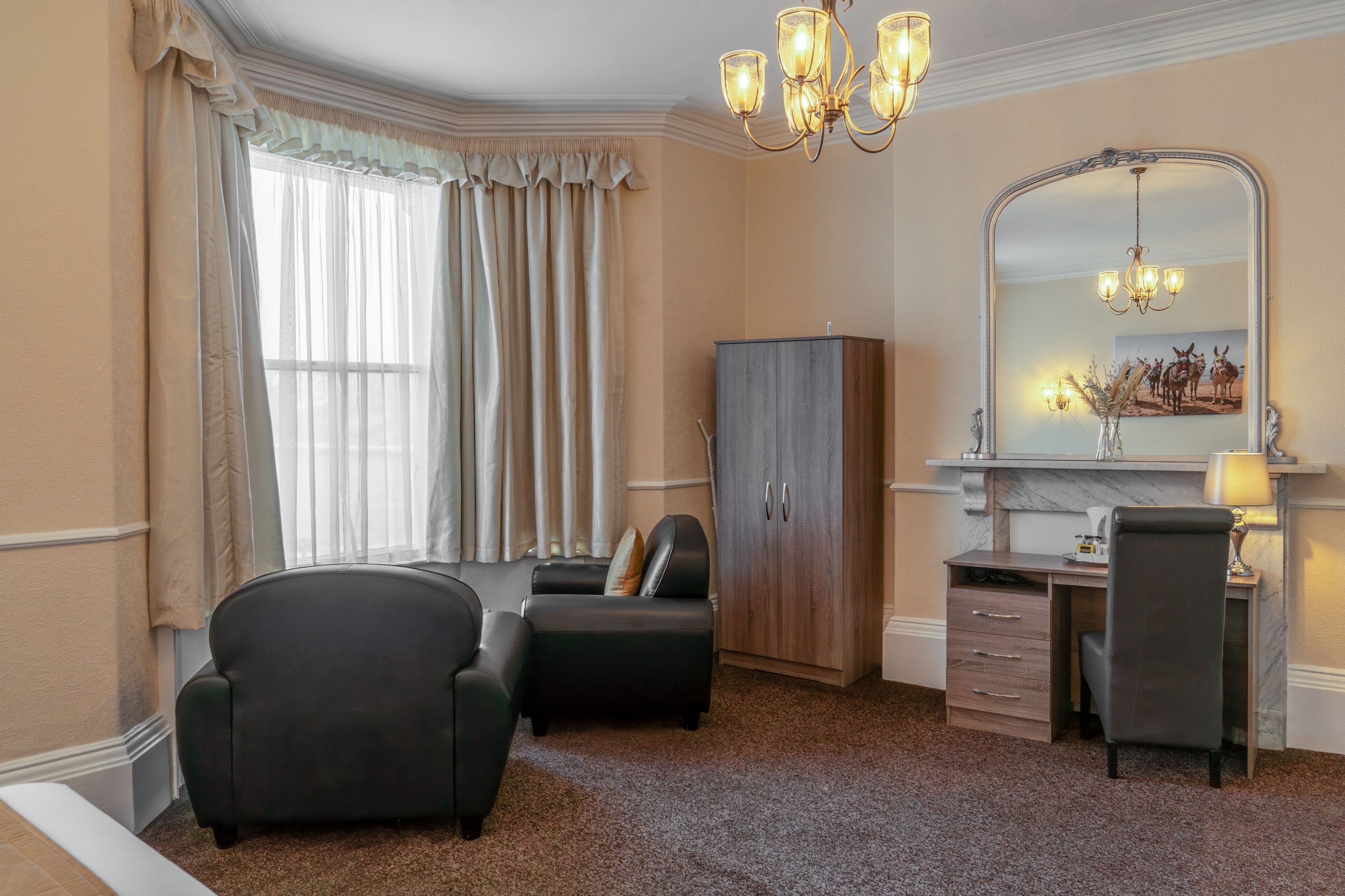 A hotel room with a large window, a desk with a chair, a wardrobe, and a mirror.