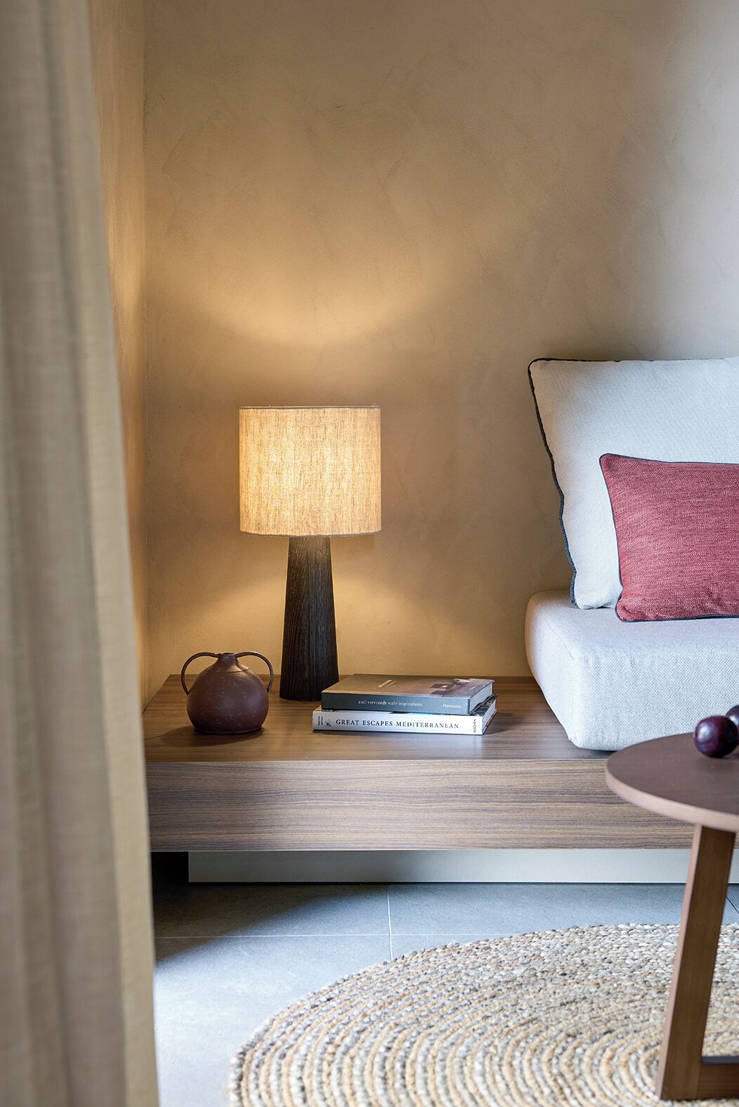 Un angolo lettura accogliente con una lampada, un libro e un vaso decorativo su un tavolino in legno.