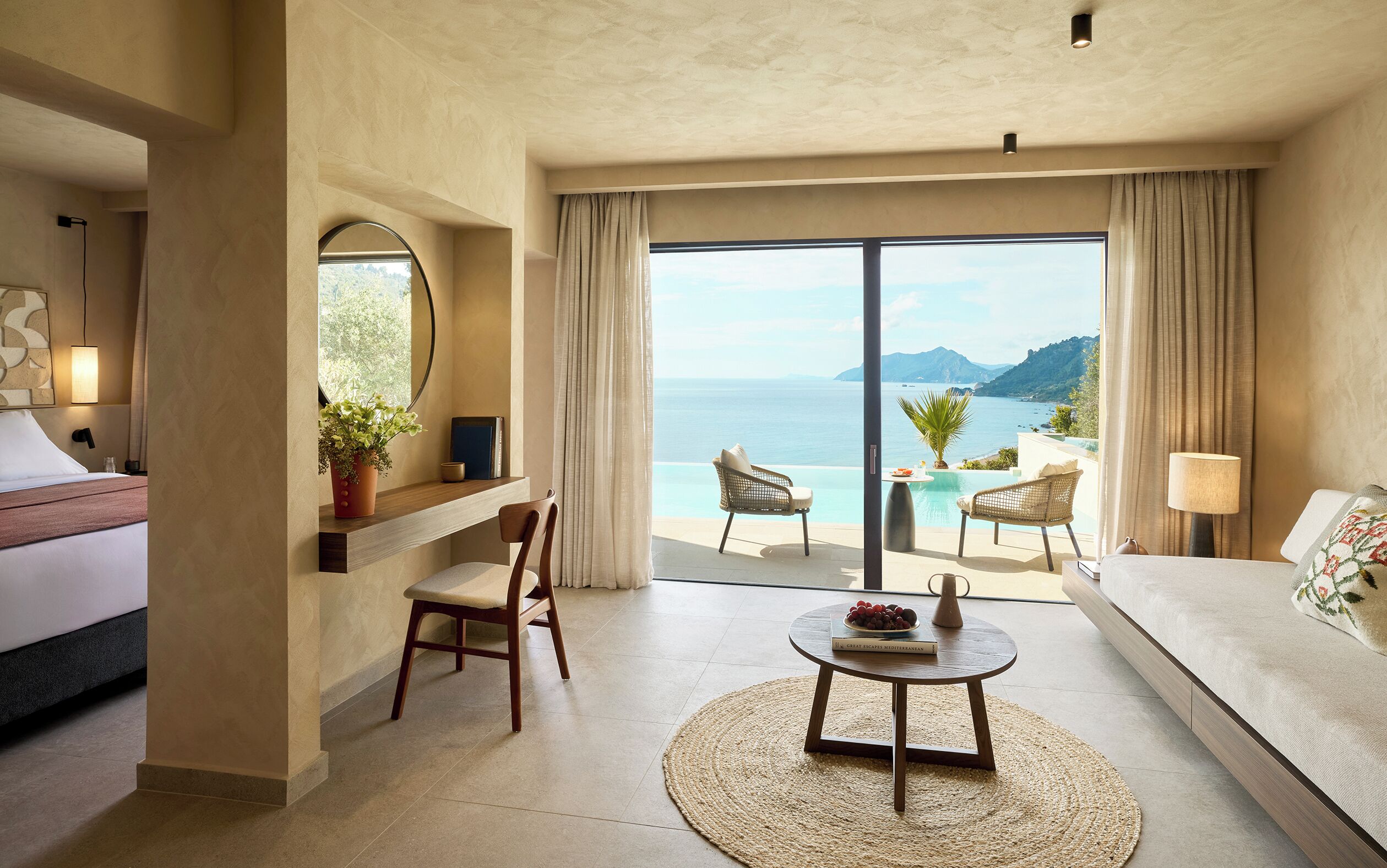 Habitación de hotel con un amplio ventanal que ofrece vistas al mar, un sofá, una mesa de comedor y una silla.