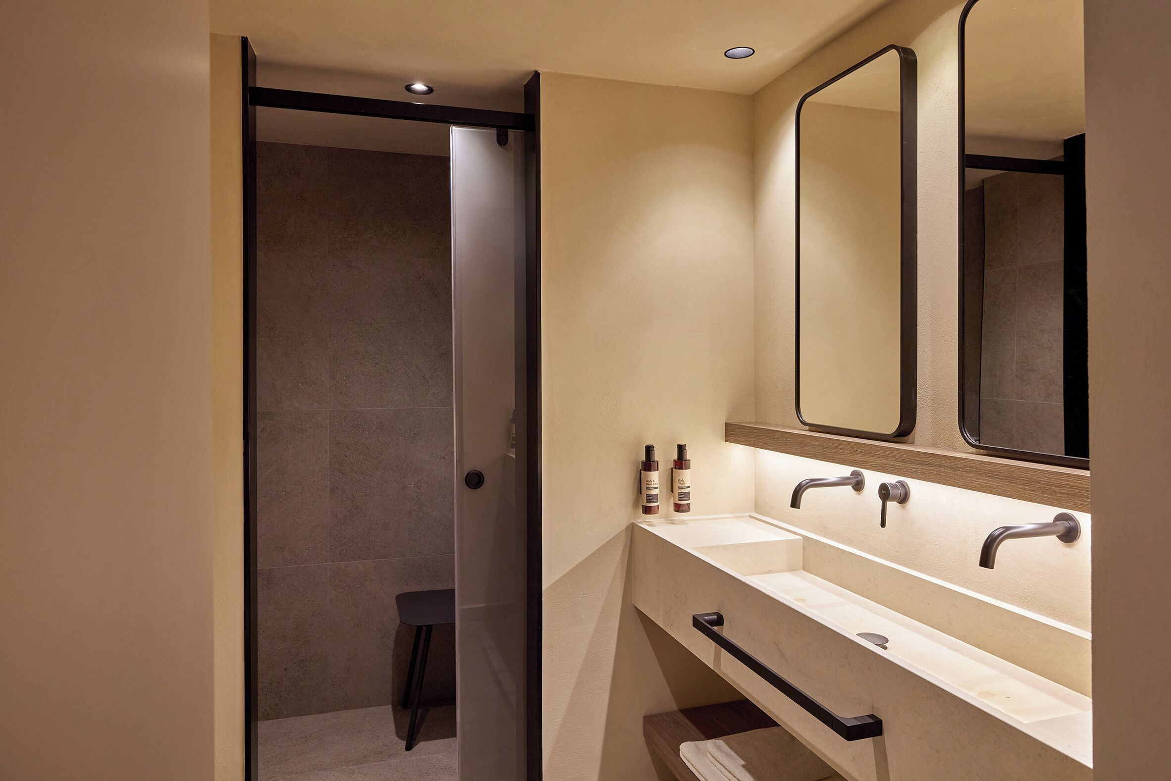 Un bagno moderno con un ampio specchio, due lavabi e una zona doccia.