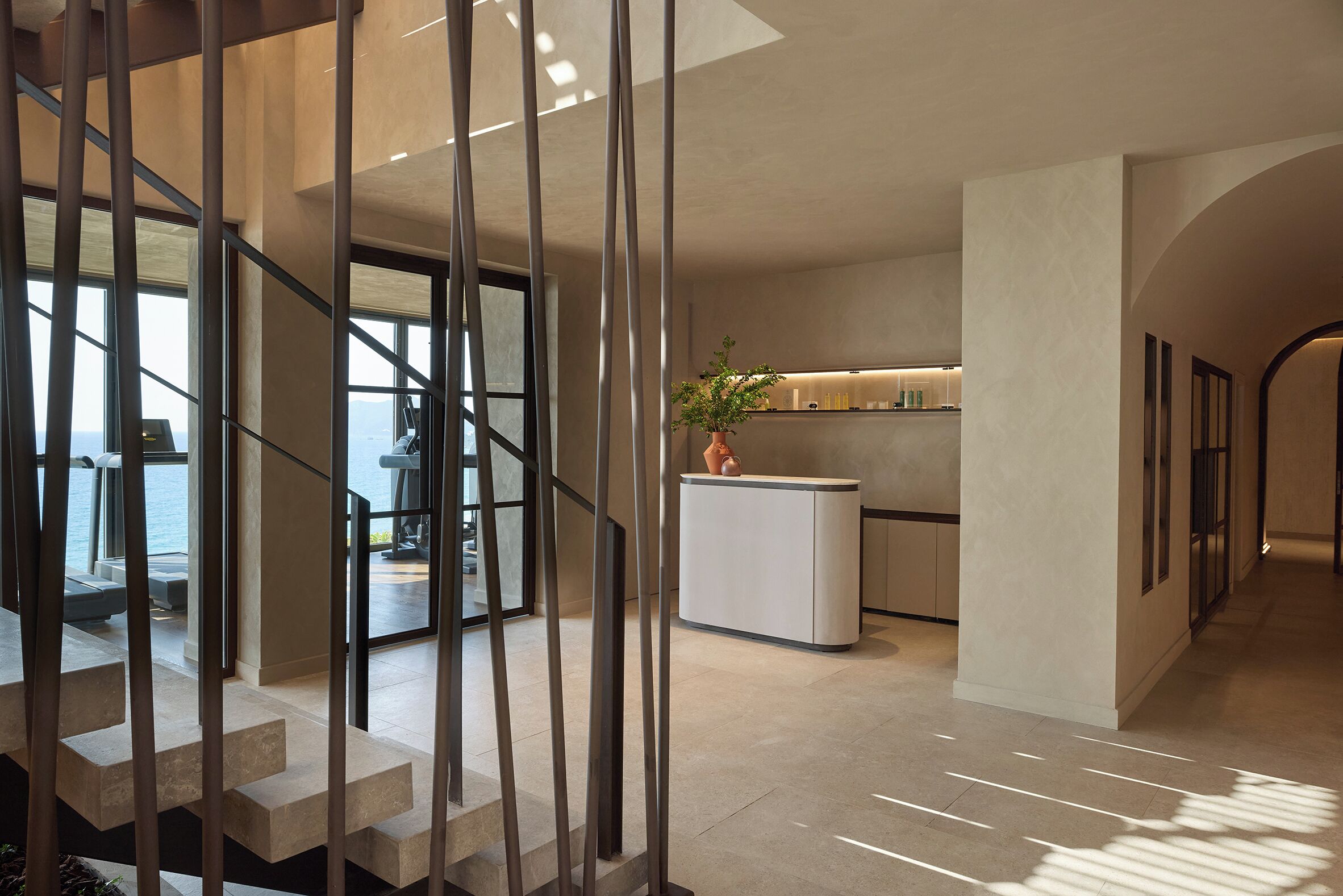 Un interior moderno con una escalera que lleva a un balcón, un mostrador de recepción y una zona de cocina.