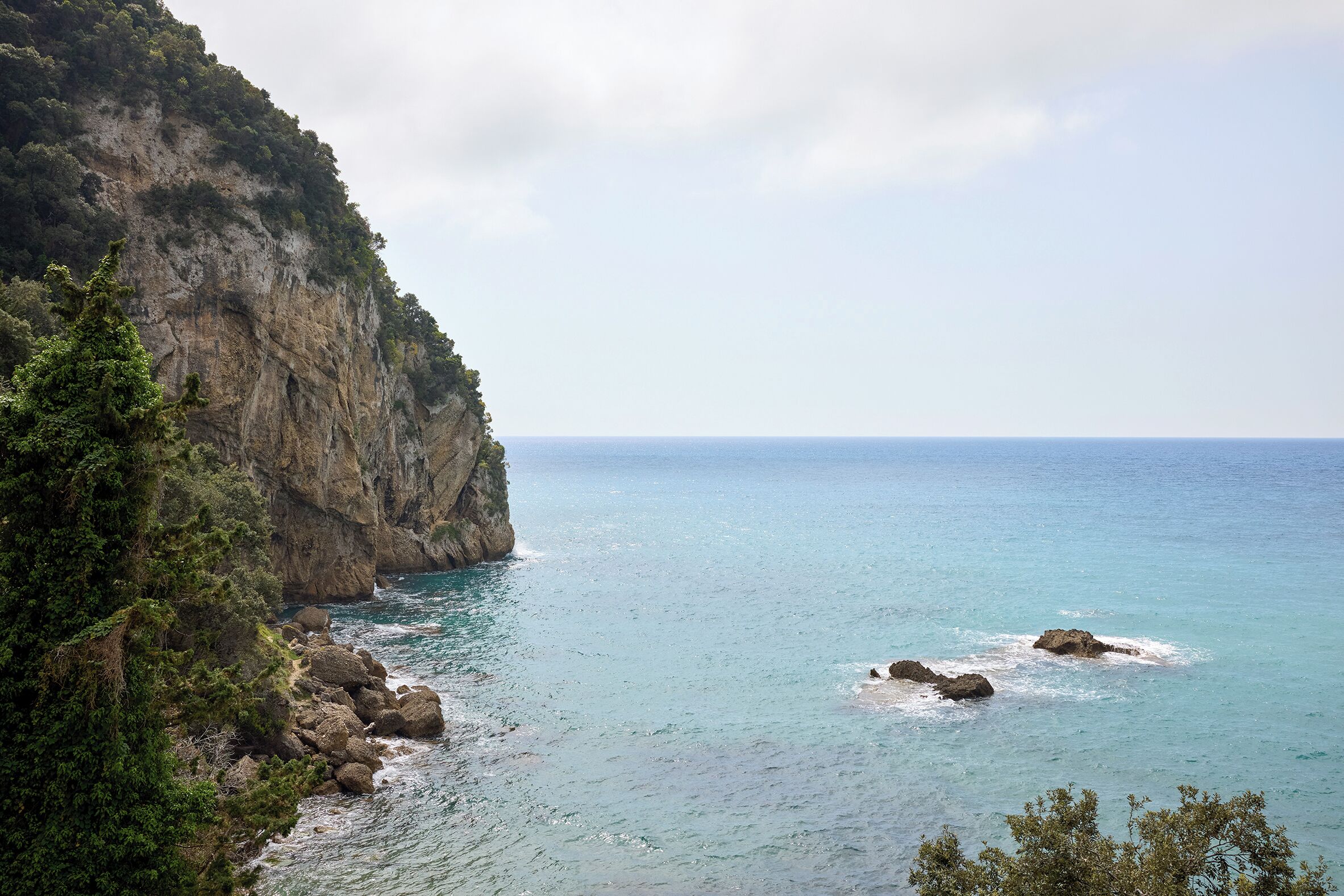 A coastal landscape with a rocky cliff and calm sea.