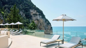 A rooftop terrace with sun loungers and umbrellas overlooking a cliff and the sea. - Ella Alkyna – Adults Only (Corfu)