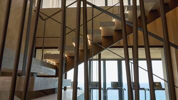 A modern interior with a staircase leading to a balcony overlooking the sea.