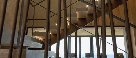 Un interior moderno con una escalera que lleva a un balcón con vistas al mar.