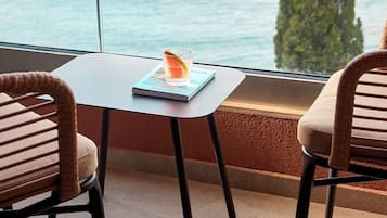 A modern room with a view of the sea, featuring two wicker chairs, a small table with a book and a glass of water, and a large window.