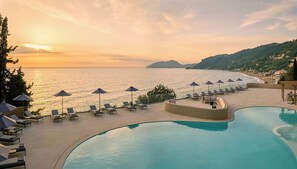 A resort with a pool, sun loungers, umbrellas, and a view of the sea at sunset. - Ella Alkyna – Adults Only (Corfu)