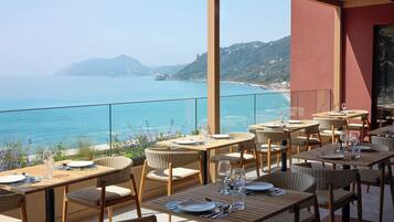 Un área de comedor al aire libre con mesas y sillas, con vistas a la costa.