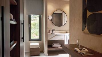 Une salle de bain moderne avec un lavabo intégré, un miroir rond et une fenêtre donnant sur un espace verdoyant.