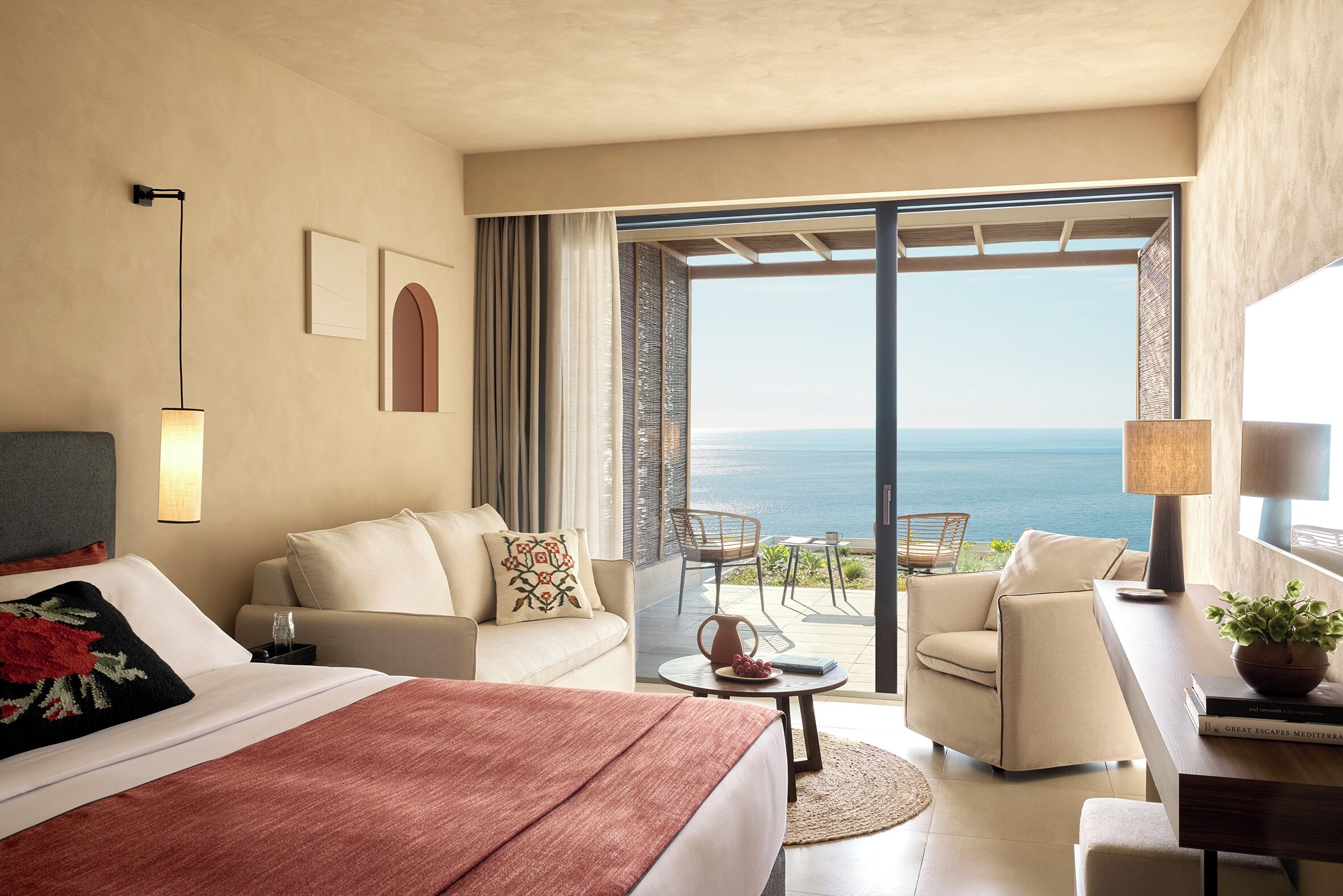 A hotel room with a bed, a sofa, a desk, and a view of the sea.