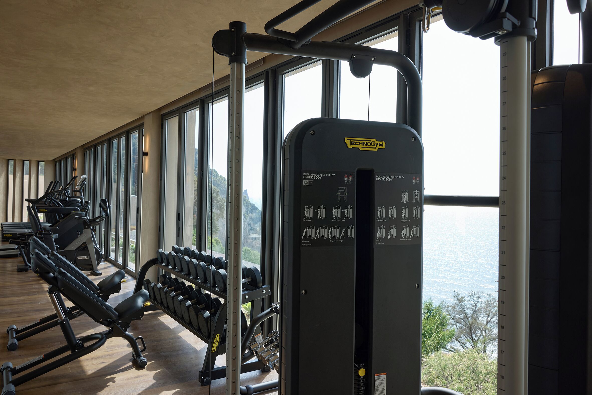 A gym with exercise equipment, large windows, and a view of the outdoors.