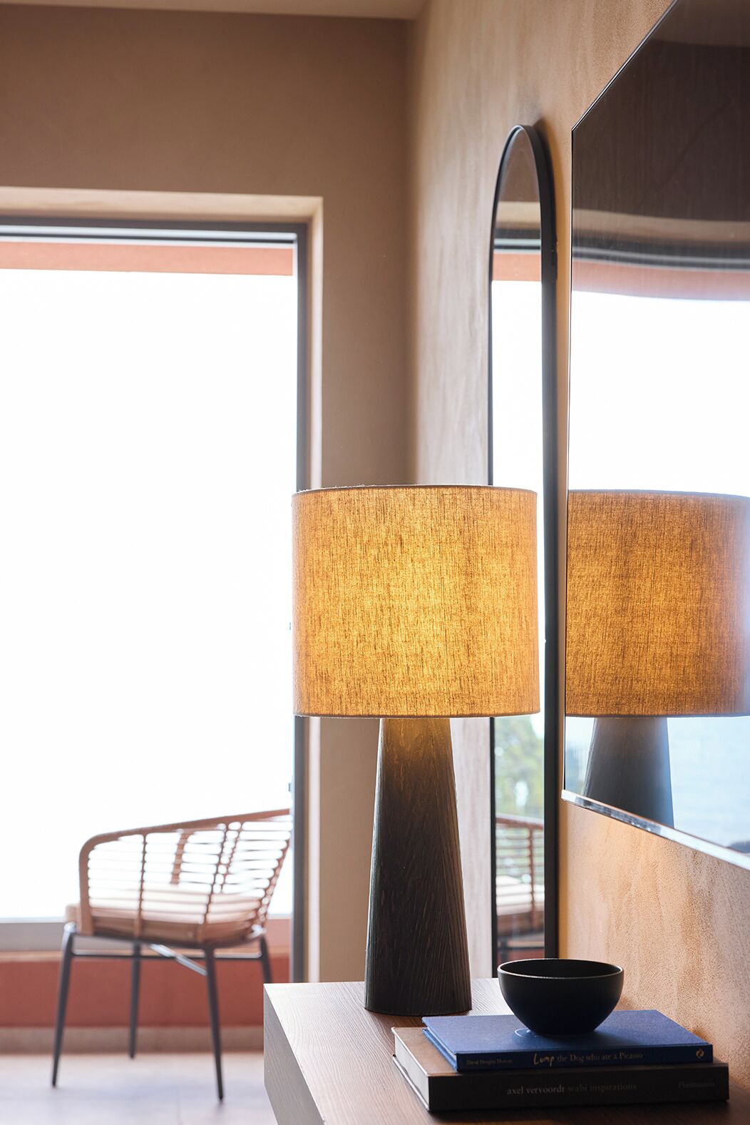 A modern room with a tall floor lamp, a wooden side table, a black bowl, and a chair near a large window.