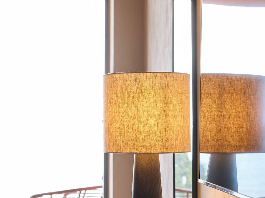 A modern room with a tall floor lamp, a wooden side table, a black bowl, and a chair near a large window.